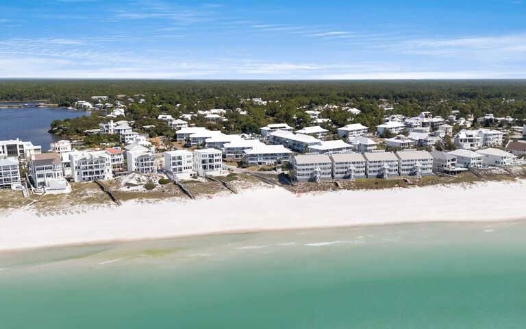 Aerial view of beachfront properties nestled along pristine white sand and emerald waters, surrounded by lush coastal forest.