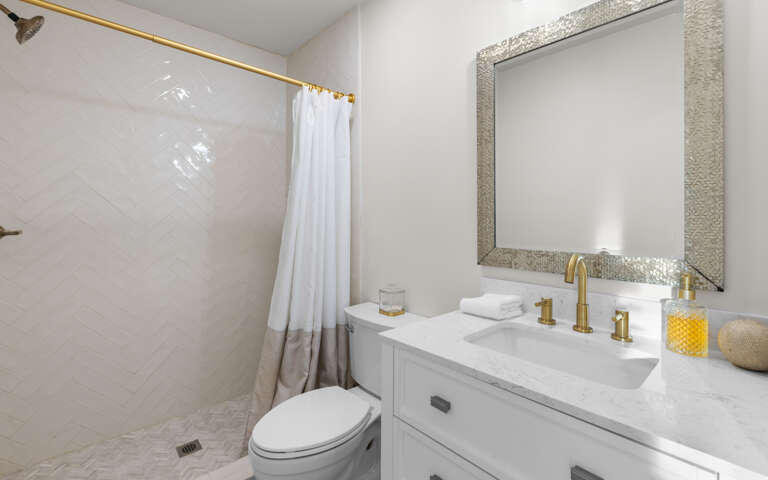 Unwind in your elegant bathroom featuring marble countertops, gold fixtures, and a refreshing shower with crisp white linens.