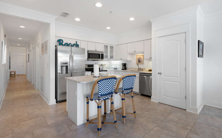 Your coastal-inspired kitchen awaits with crisp white cabinets, stainless appliances, and stylish blue-striped stools perfect for morning coffee.