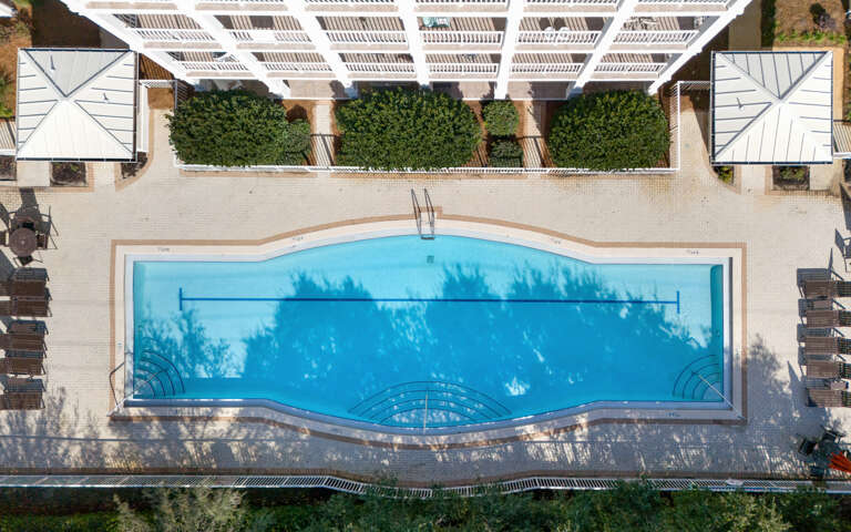 Aerial view reveals the property's stunning swimming pool surrounded by sun loungers and lush greenery, creating an inviting outdoor oasis.