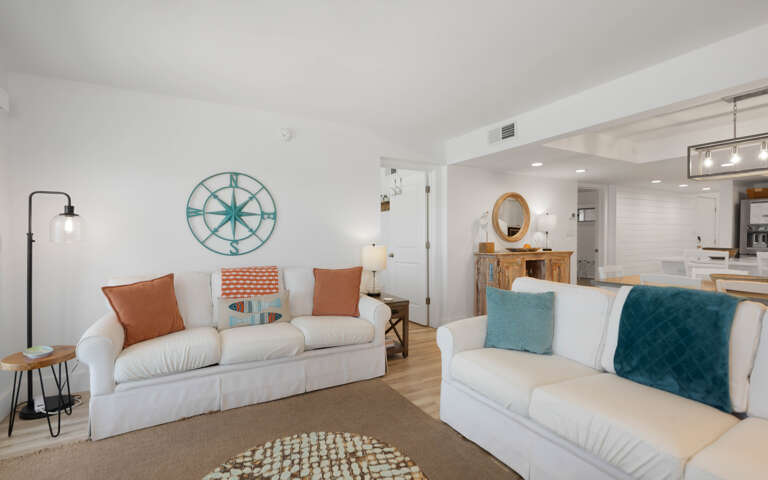 Sink into plush white sofas adorned with coastal-inspired pillows, where nautical charm meets modern comfort in your bright, airy retreat.