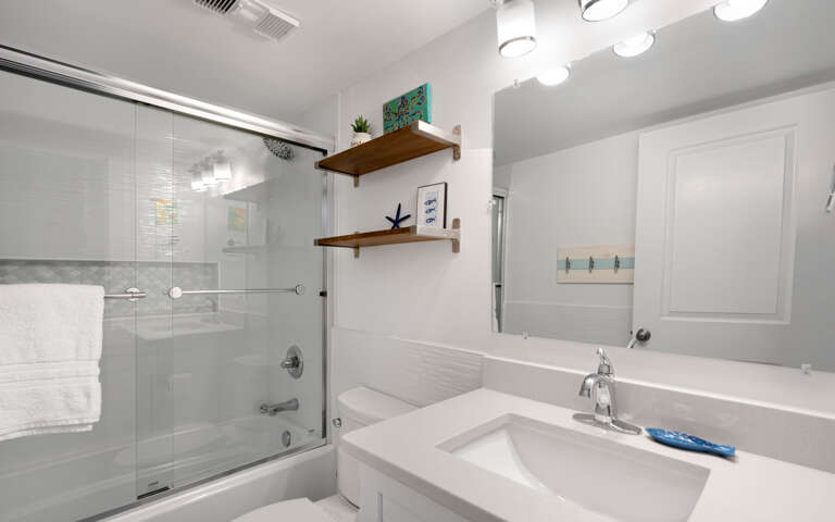 Unwind in your pristine bathroom featuring a glass-enclosed tub-shower combo and stylish vanity with thoughtful coastal touches.