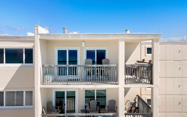 Modern beachside property featuring spacious balconies with gulf-facing views and comfortable outdoor seating under clear blue skies.