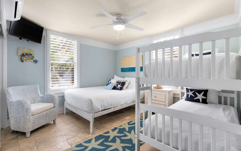 Your coastal-themed bedroom features crisp white bunk beds and nautical decor, creating a serene retreat where ocean breezes flow through plantation shutters.