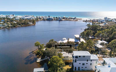 Stunning aerial view captures waterfront homes nestled between tranquil bay waters and pristine coastline, showcasing the peaceful lakeside community setting.