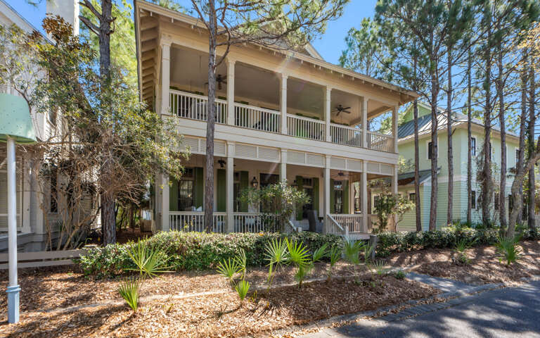 Charming coastal home with wraparound porches nestled among towering pines and native landscaping in a peaceful neighborhood setting.