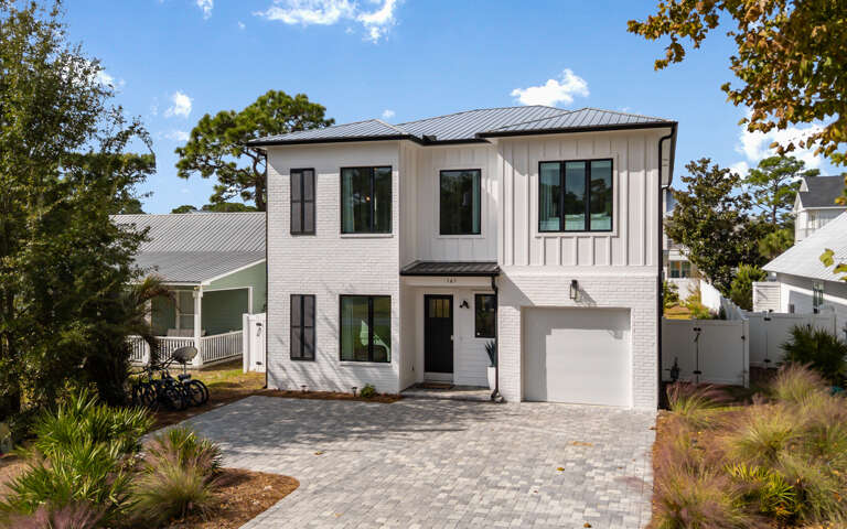 White Two-story Residence Under Blue Skies, Bordered By Green Grass And Gray Gravel Driveway