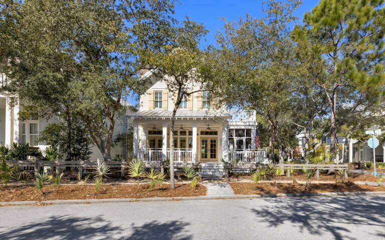 Charming two-story coastal home with wraparound porch and mature tree canopy on peaceful residential street.