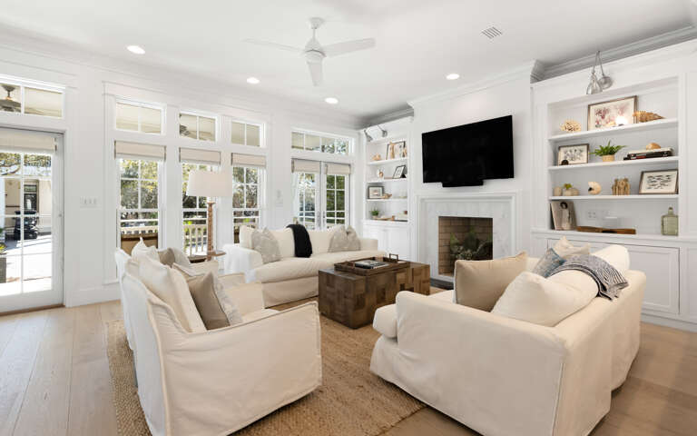 Sink into plush white sofas by the fireplace where natural light floods through elegant French doors, creating your perfect retreat.