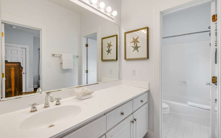Your pristine bathroom features a spacious vanity with fresh towels, elegant nautical artwork, and bright vanity lighting for your morning routines.