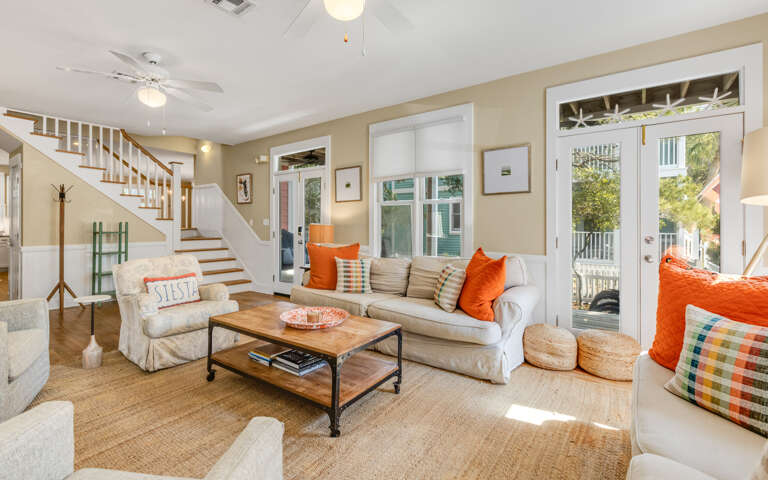 Relax in your bright, airy living room with vibrant orange accents and comfortable seating that opens to outdoor spaces.