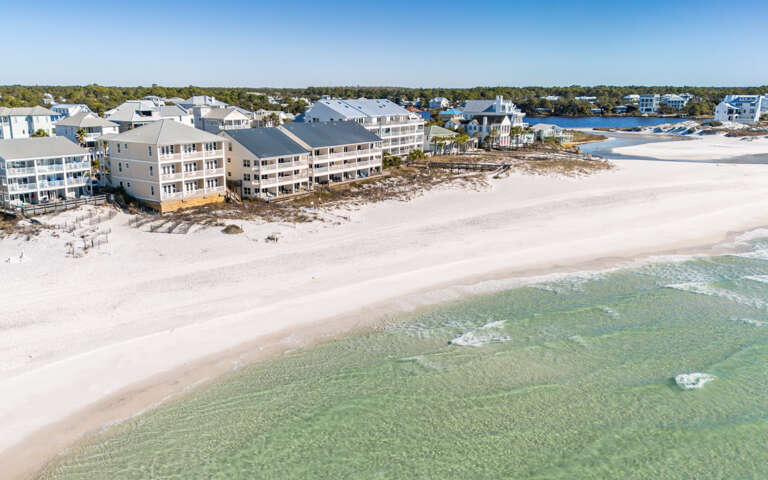 Aerial view of beachfront vacation rental properties situated directly on pristine white sand beach with crystal-clear emerald waters.
