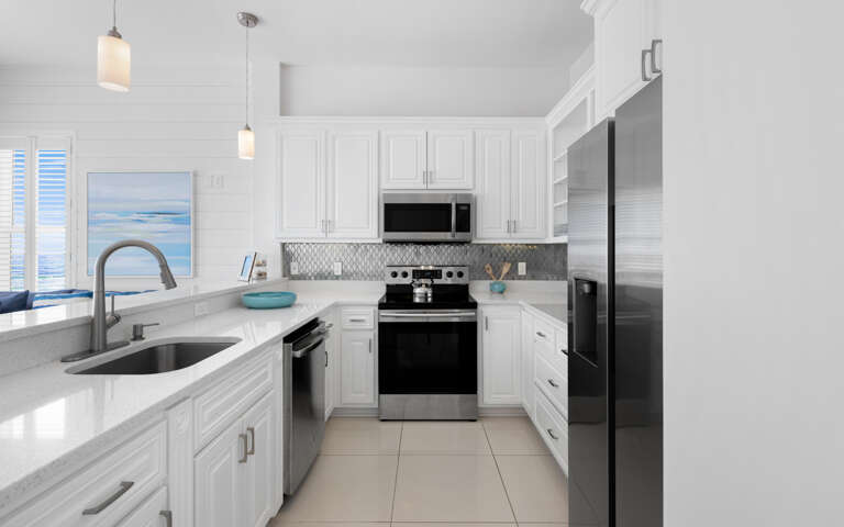 Your modern kitchen awaits with gleaming countertops, stainless appliances, and ocean artwork that sets a coastal mood for preparing meals.