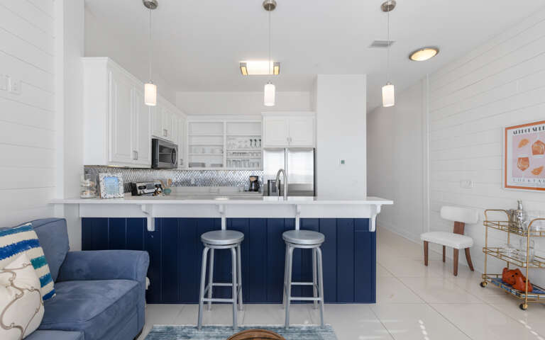 Your sleek kitchen features navy blue island seating, modern pendant lighting, and stainless steel appliances for effortless meal prep.