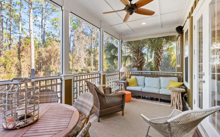 Screened Porch Area Of A Vacation Rental With Seating And Forest View