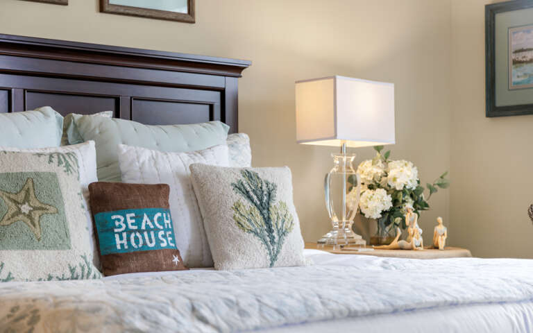 Bedside Blooms Beside Blue Beach House Pillow On Plush Bed