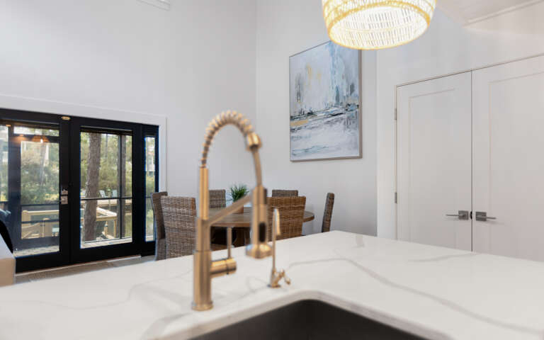 Cook and dine in style with marble countertops, elegant gold fixtures, and natural light streaming through French doors.