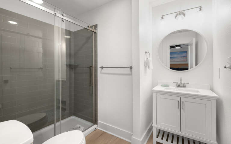 Your private bathroom features a spacious glass shower, elegant vanity, and coastal artwork that creates a spa-like retreat.