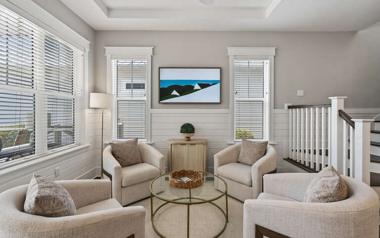 Sink into plush neutral armchairs around your glass coffee table, where natural light streams through elegant blinds.