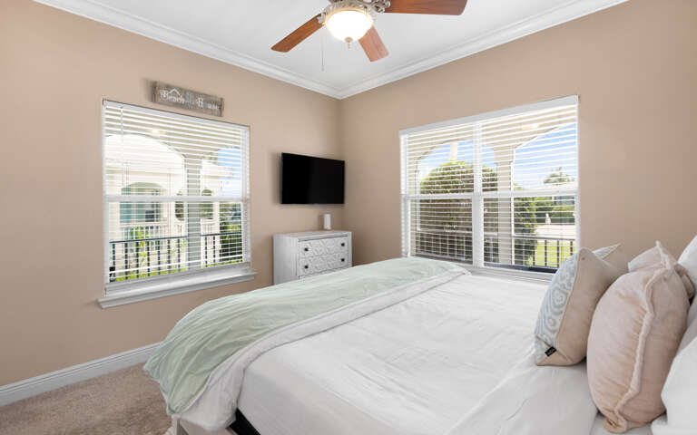 Bedroom With Beige Walls, Big Bed Beneath Bright Windows, Ceiling Fan Above