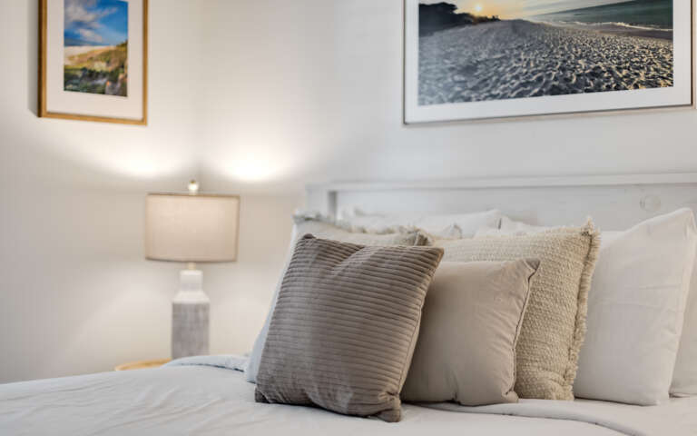 Sink into plush pillows and soft linens in your serene bedroom retreat, where coastal artwork and warm lighting create the perfect ambiance for restful nights.