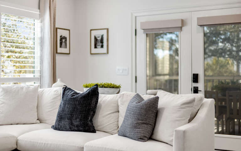 Sink into this plush white sectional where natural light streams through plantation shutters, creating your perfect afternoon reading nook.