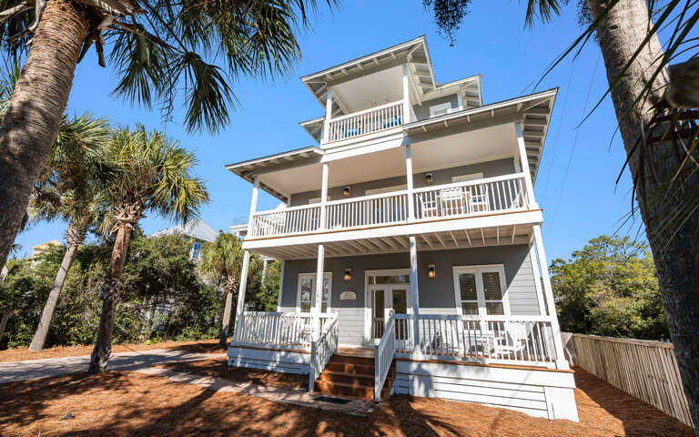 Charming coastal property with multiple levels of wrap-around porches surrounded by tropical palm trees.
