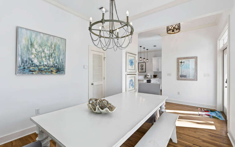Gather around your elegant dining table beneath the stunning chandelier, where coastal artwork and warm hardwood floors create the perfect setting for memorable meals.