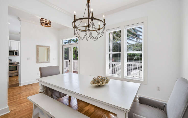 Gather around your elegant dining table where warm wood floors meet crisp white walls and natural light streams through French doors.