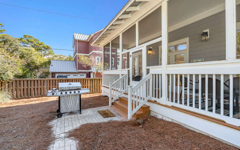 Modern vacation home exterior features covered porch with white railings and private fenced yard with grill for outdoor entertaining.