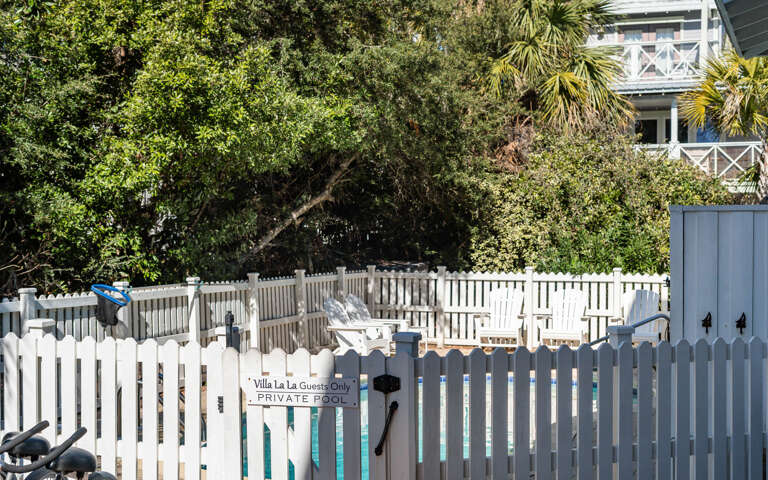 Private pool area surrounded by tropical landscaping and classic white picket fencing, creating an exclusive outdoor retreat.
