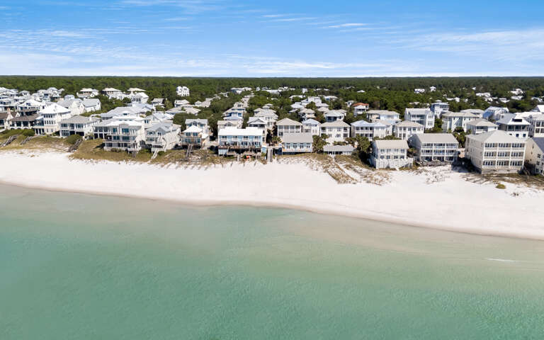 Stunning aerial view reveals pristine beachfront homes along white sand and turquoise waters in this coastal community.