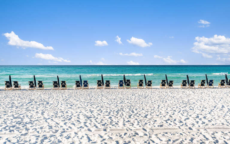 Beach With Black Chairs, Blue Sea, And White Sand