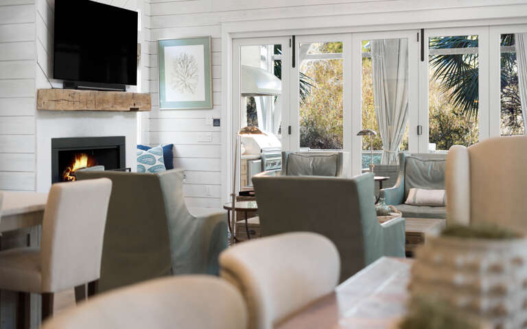 Relax in your bright living space with crackling fireplace, wall-mounted TV, and cozy seating overlooking tropical gardens.