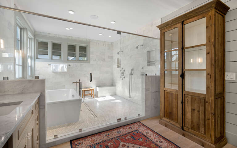 Your spa-like bathroom features a luxurious soaking tub and spacious walk-in shower with marble accents and rustic wood storage.