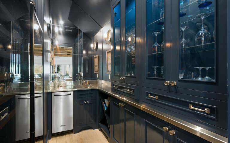 Step into your elegant butler's pantry with custom navy cabinetry, gleaming brass fixtures, and glass displays for your entertaining essentials.
