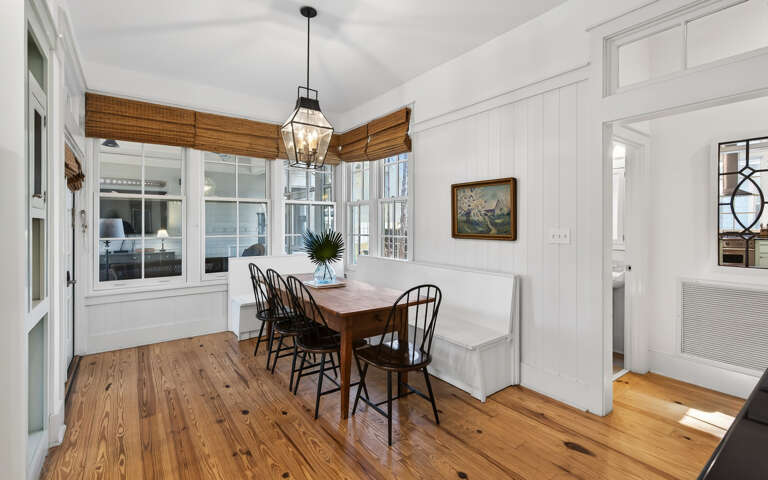 Your charming dining nook features rustic wood floors, classic Windsor chairs, and warm natural light streaming through bamboo shades.