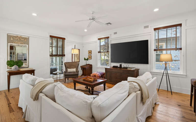Unwind in this elegant living room with plush white sofas, warm hardwood floors, and modern entertainment setup for your perfect retreat.