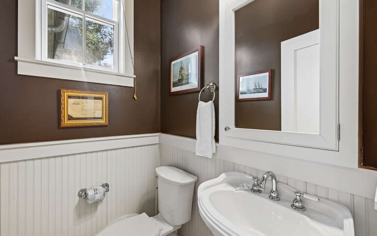 Step into your charming bathroom with classic wainscoting, nautical artwork, and a crisp white vanity that creates the perfect coastal retreat.