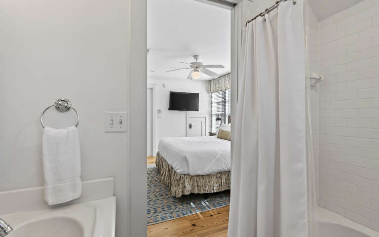 Step from your pristine white bathroom into your cozy bedroom, where crisp linens and warm wood floors create the perfect retreat.