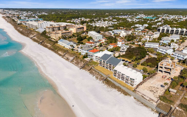 Aerial view of beachfront community with pristine white sand beaches and turquoise waters along the coastline.