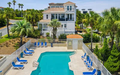 Luxurious three-story Mediterranean villa features private pool surrounded by palm trees in tropical setting.