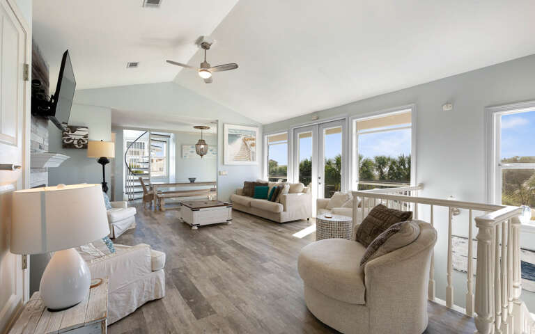 Relax in your bright, coastal-inspired living space with panoramic windows framing tropical views and comfortable seating perfect for unwinding.