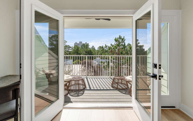 Step onto your private balcony where wicker seating awaits, framing peaceful treetop views and endless sky.