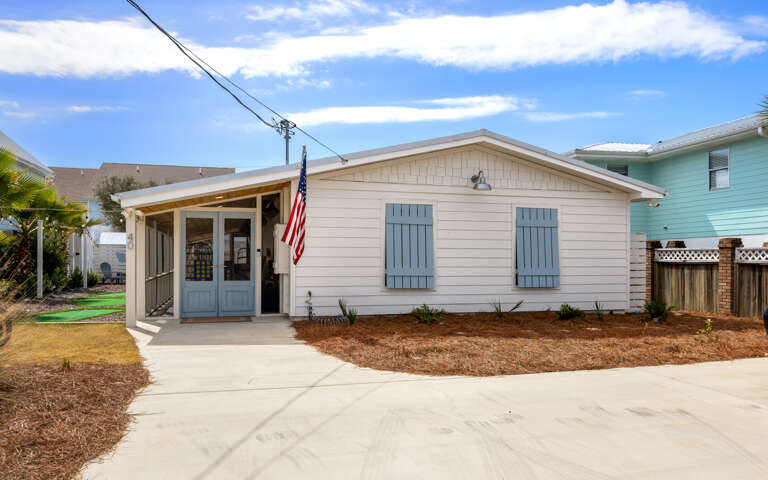 Charming beachside cottage with blue shutters and welcoming front porch in a quiet coastal neighborhood.