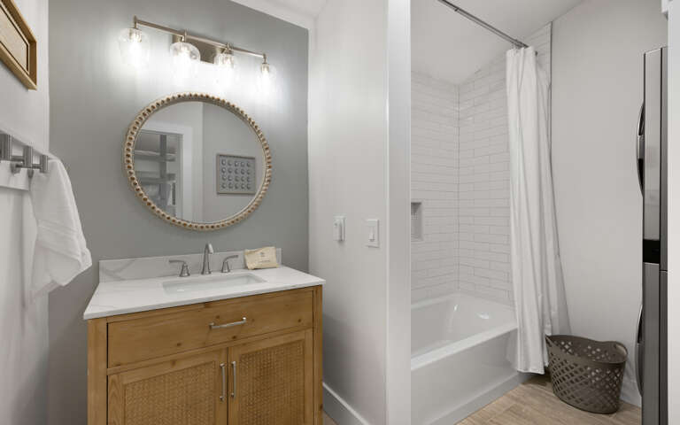 Step into your stylish bathroom featuring a warm wood vanity, elegant round mirror, and refreshing tub-shower combo for unwinding after adventures.