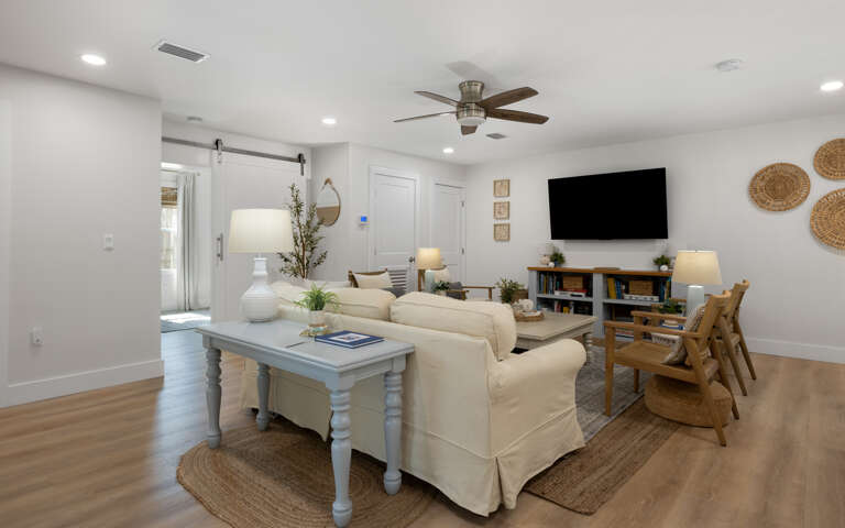 Unwind in your bright, modern living room with cozy seating, entertainment center, and coastal touches throughout.