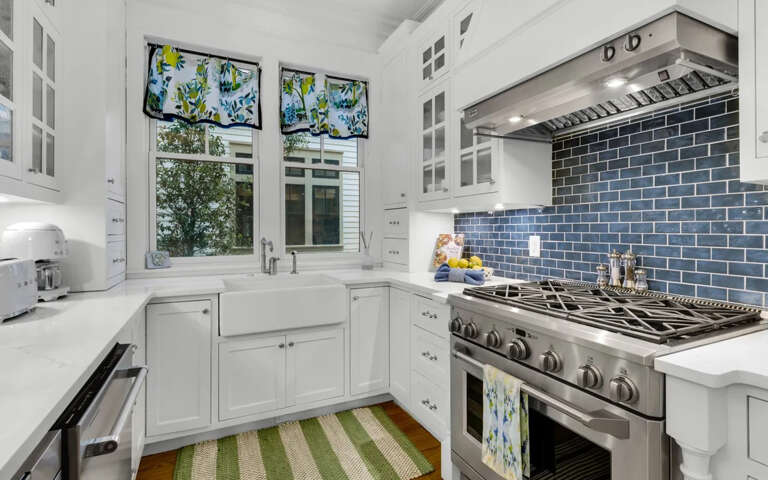 Your bright, airy kitchen features pristine white cabinetry, professional-grade stainless steel appliances, and a stunning blue subway tile backsplash that catches the natural light.