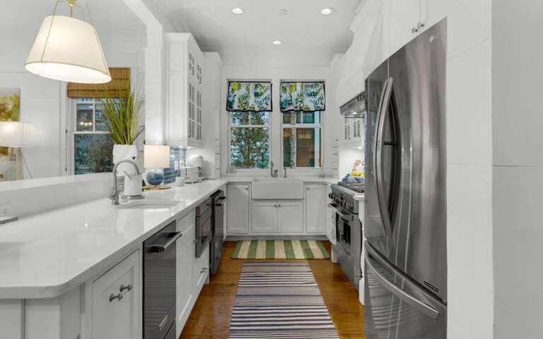 Prepare meals in this bright, modern kitchen featuring stainless steel appliances, quartz countertops, and abundant natural light from cheerful garden windows.