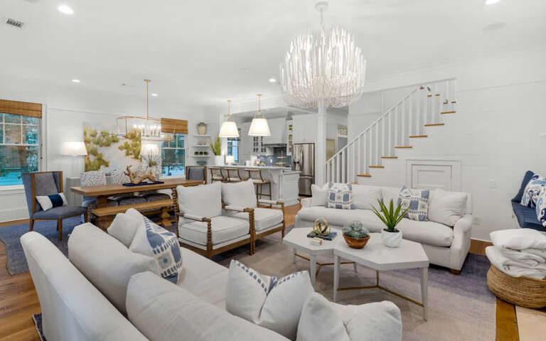 Relax in your spacious open-plan living area, where coastal elegance meets comfort with plush seating and a stunning chandelier overhead.
